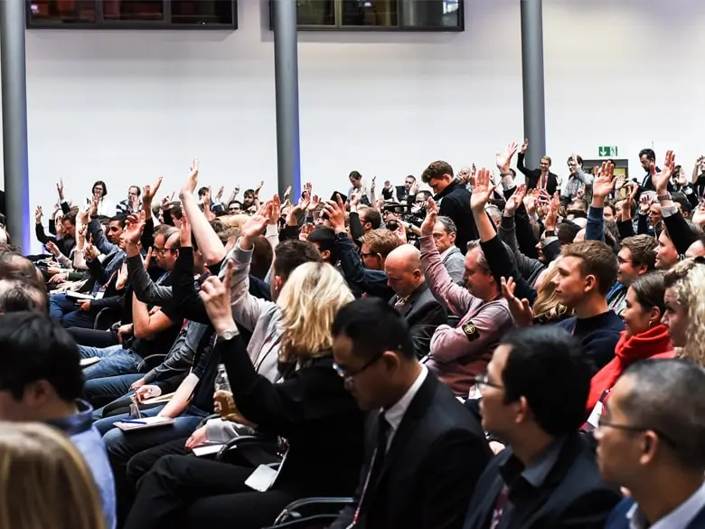 Seated audience at a conference raising their hands to ask questions