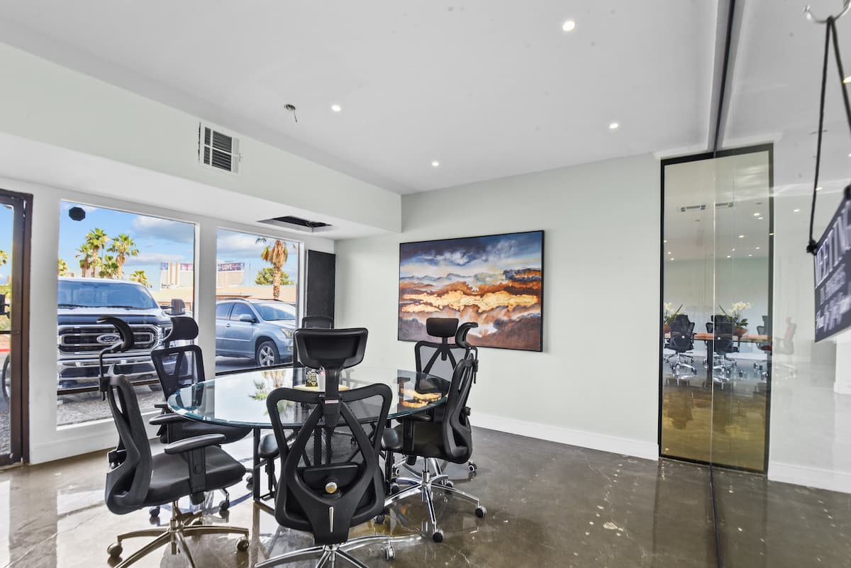 Conference Room I: round glass table with black ergonomic chairs, a landscape painting and street-facing windows