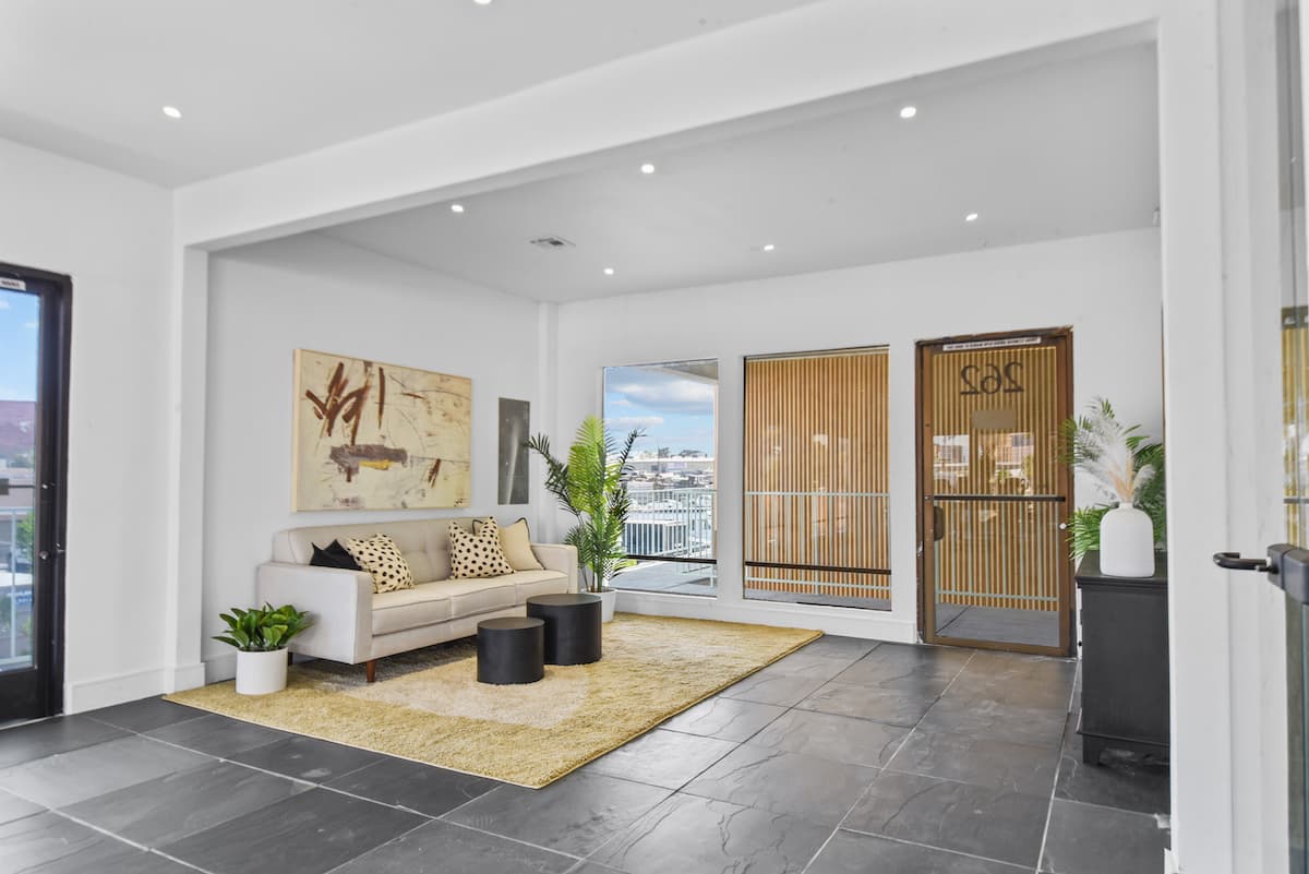 Suite 262 reception with a beige sofa, black side tables, a gold rug and a wood-slat entry