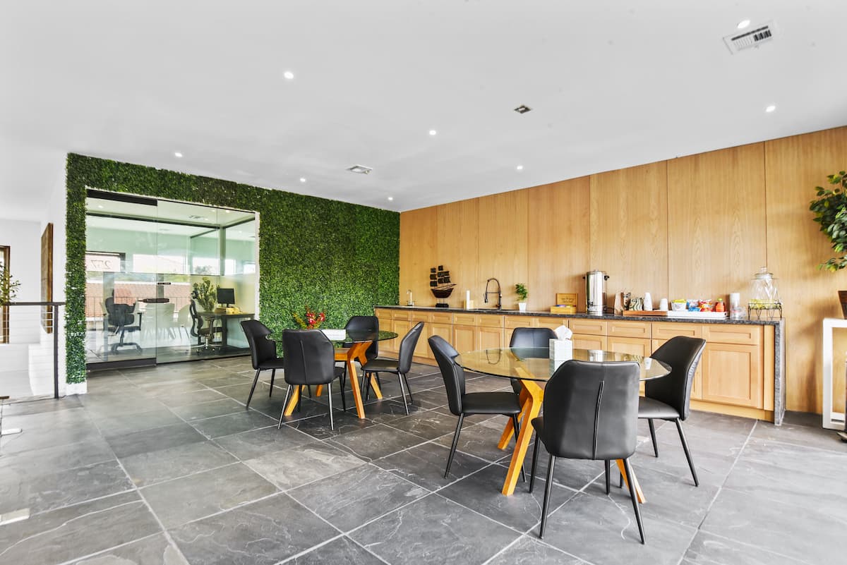 Zona de descanso con un muro vegetal, una pequeña cocina con paneles de madera y mesas de cristal con sillas negras