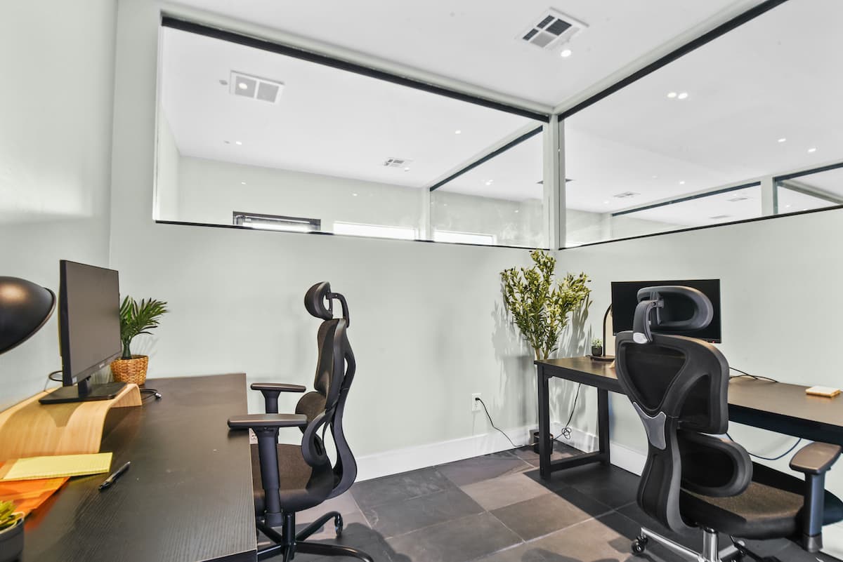 Private office for two with black desks, monitors and ergonomic chairs behind a glass partition