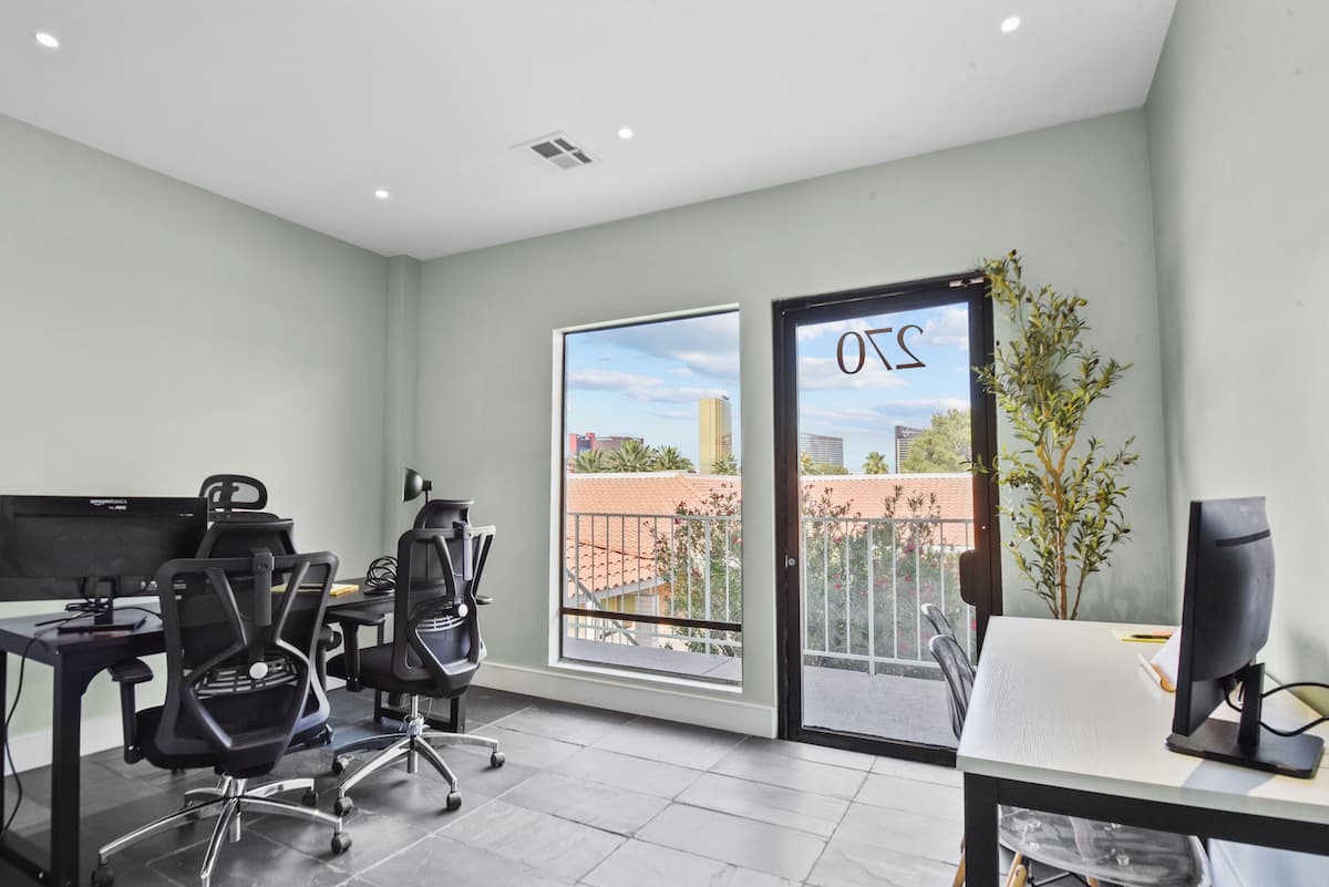Suite 270 private office with two desks, ergonomic chairs and a door onto a balcony with Strip views
