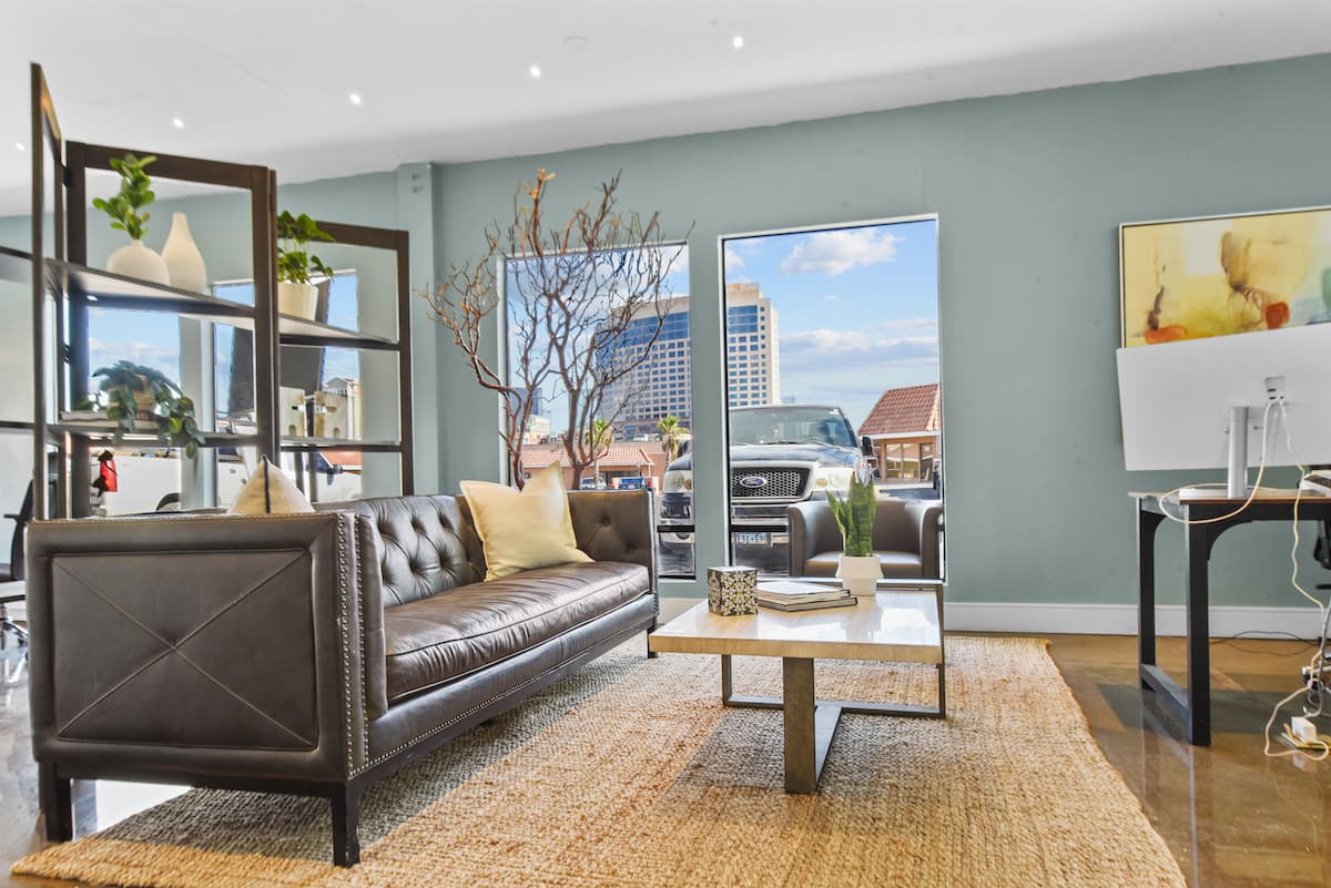 Sage-walled lounge with a tufted leather sofa, jute rug and travertine coffee table in front of large windows