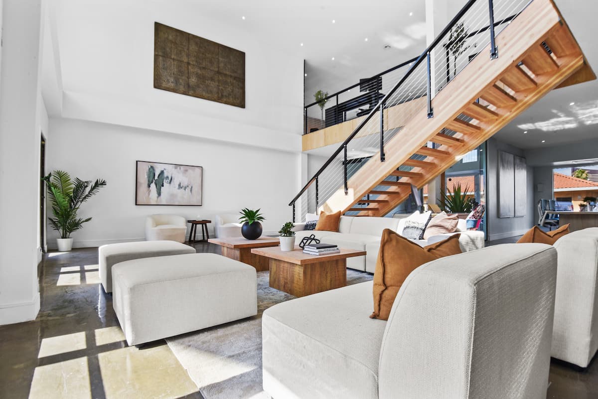 Double-height lounge with cream sectional seating, wood coffee tables and a floating timber staircase